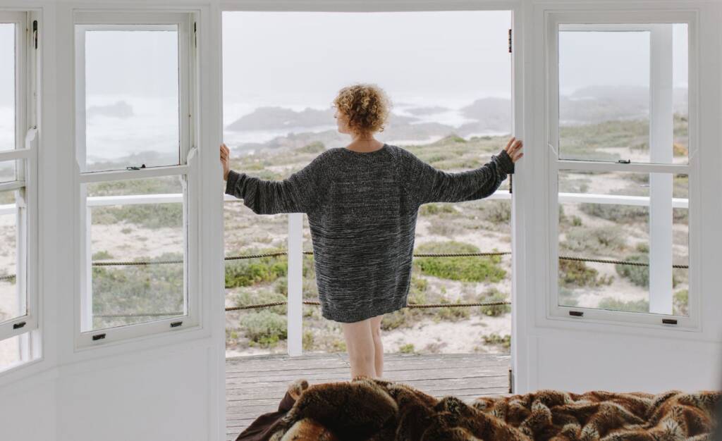 woman at open door looking at beach landscape