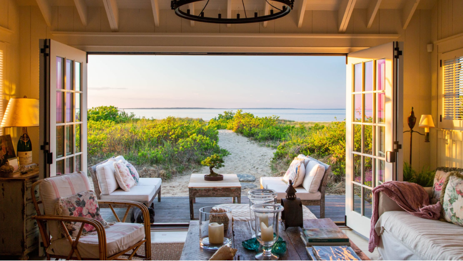 coastal cottage style home with open french doors looking out to a sandy pathway to the ocean