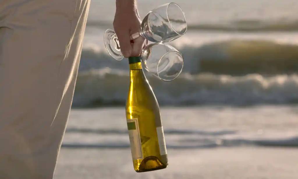 Bottle of Chardonnay and two glasses  by the ocean waves