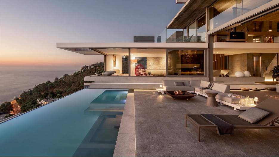 sleek, contemporary oceanfront home with infinity pool overlooking rocky coastline at sunset