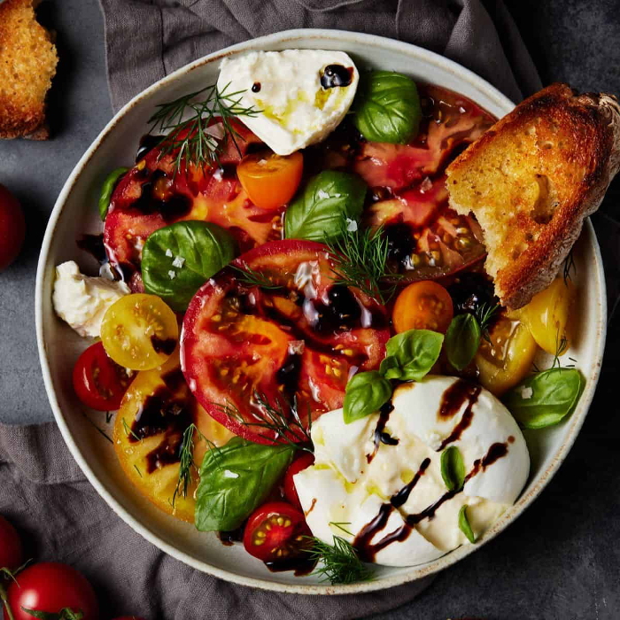 Burrata Caprese plated in a large bowl with toasted French bread, heirloom tomatoes, creamy burrata cheese, and basil.