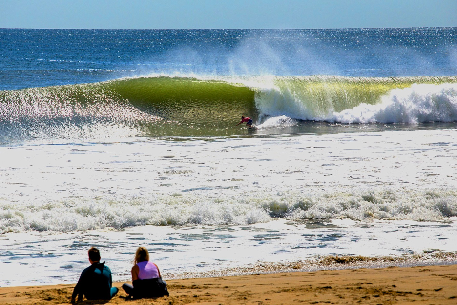 People on the sandy beach watching a surfer ride a big wave in Belmar, New Jersey