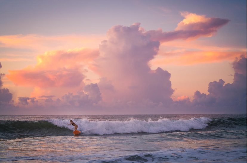 Surfer riding the waves in Wrightsville Beach, North Carolina, with a surreal sunrise and white-capped waves in the backdrop