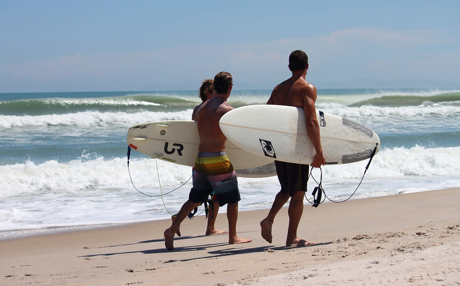 Surfers carrying their boards on the sands of Cocoa Beach, FL, with waves crashing in background