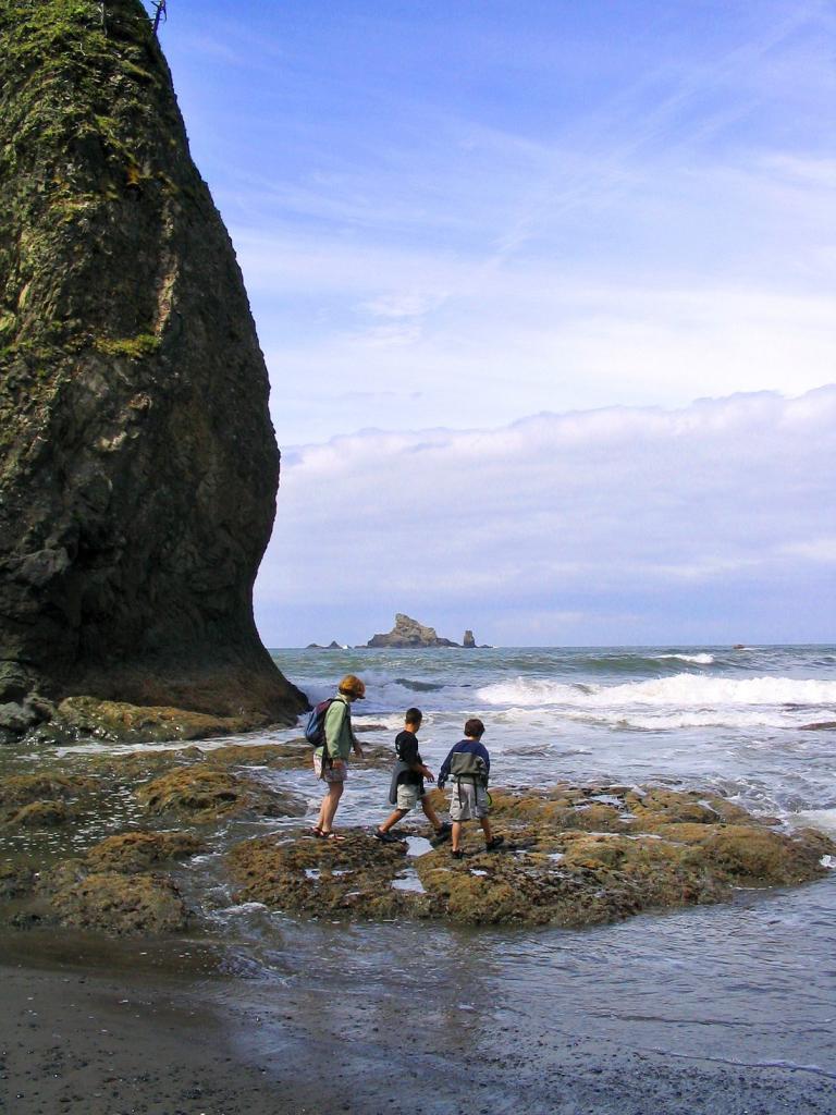 People walking on the rocks into the ocean atRialto Beach, Olympic National Park, Washington, with huge seastack in background