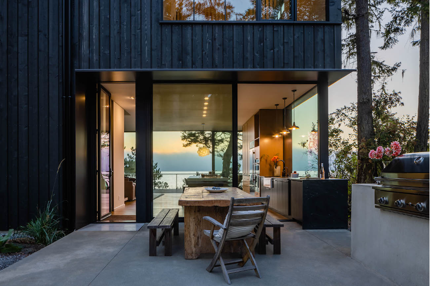 Seamless view from outdoor dining area into the kitchen and out to the living room deck, displaying uninterrupted vistas of the ocean waters, mountains, and Pacific Northwest landscape