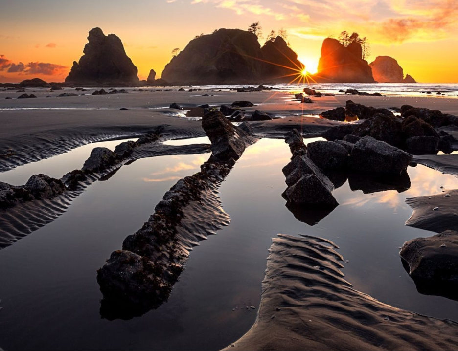 Shi Shi Beach, Makah Reservation, Washington with the Point of Arhes in the background and black rock formations in foreground, all against a brilliant sunset