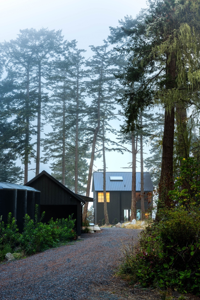 Exterior view of home's graveled entrance path, with a car port and guest cottage on site.