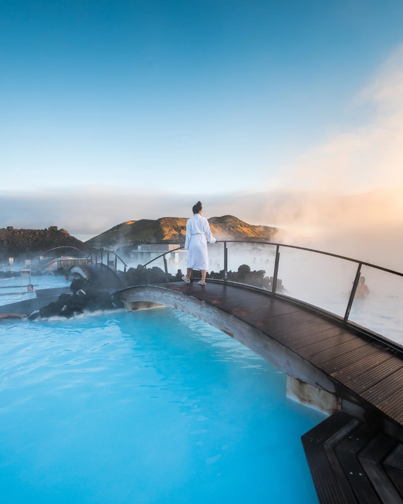 woman in bathrobe walking across a bridge over the Blue Lagoon – Grindavík, Iceland