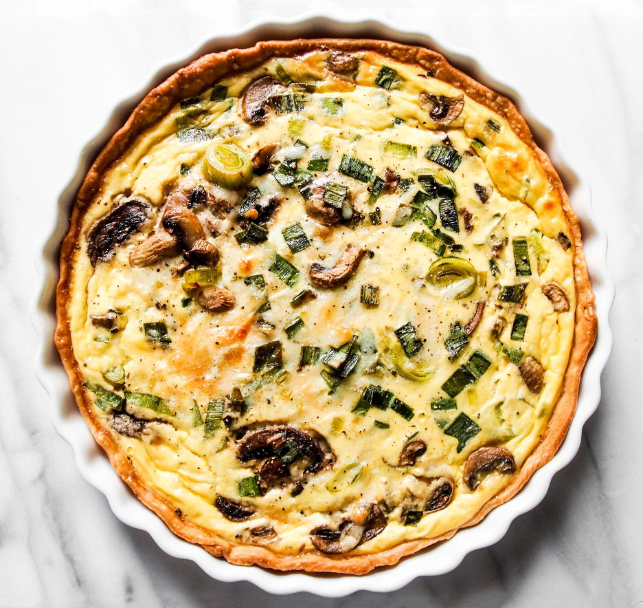 Wild Mushroom, Leek, & Gruyère Quiche in a white fluted baking dish