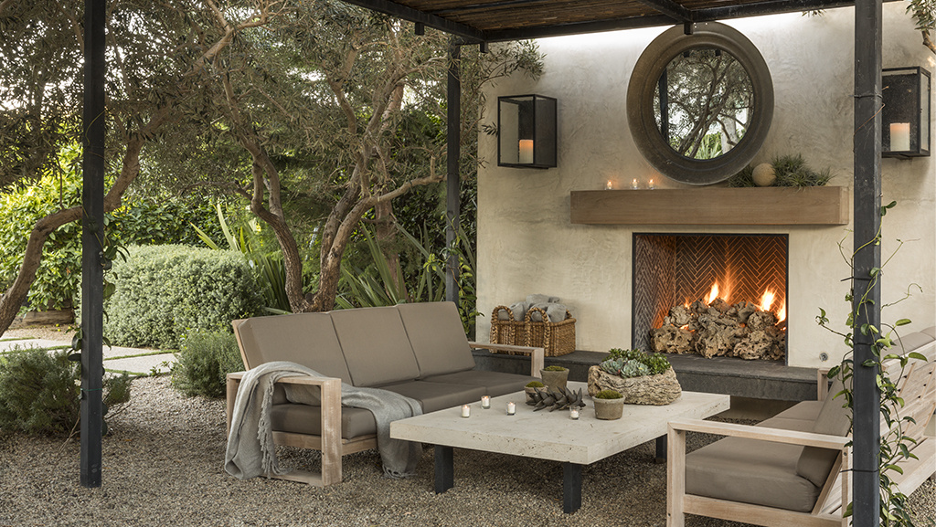 Meditative fireplace in a Garden Nook (Pacific Northwest) underneath a pergola with stone fireplace wall, rustic wood mantel, lantern sconces, and lounge seating with pavers and pea gravel 