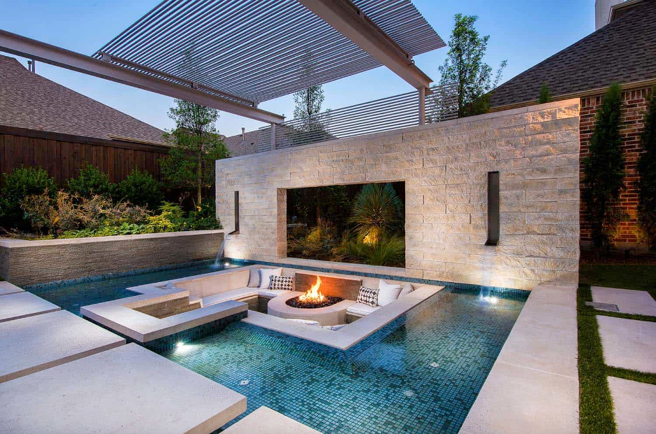 Fire and Water Pairing for Poolside Impact (Southeast Coast) Sunken firepit and lounge area implemented within the pool waters with a stone wall flanked with waterfall sconces