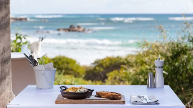 A crisp white al fresco table set for brunch in front of a breathtaking ocean view
