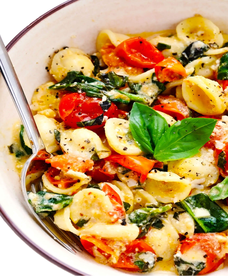 Baked Feta Pasta with Spinach and Tomatoes topped with fresh basil served in a bowl with a fork