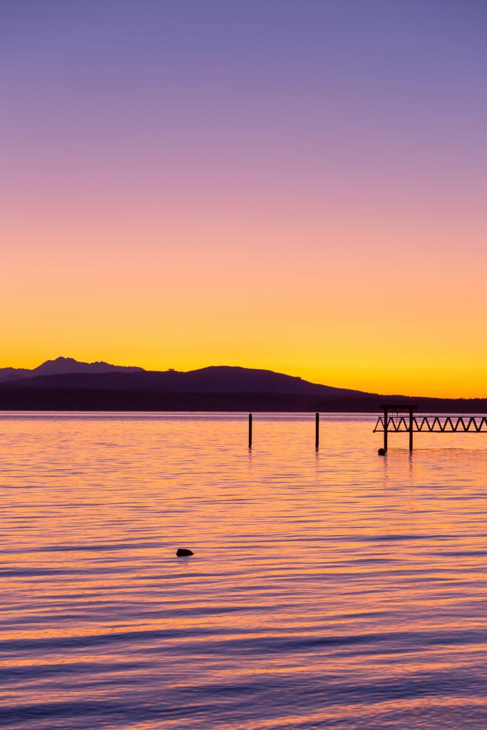 vibrant sunset across the water with mountain range in the backdrop