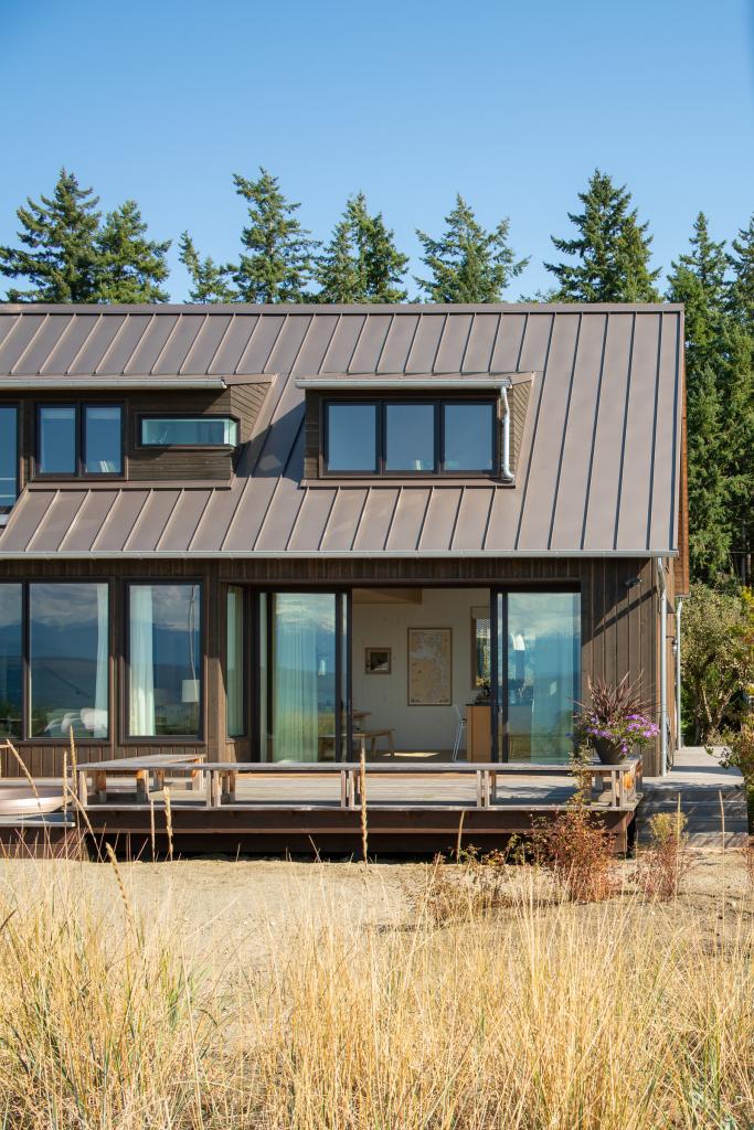 Daylight exterior shot looking from beach to the deck and the open sliding doors to the kitchen. Seagrass in the foreground.