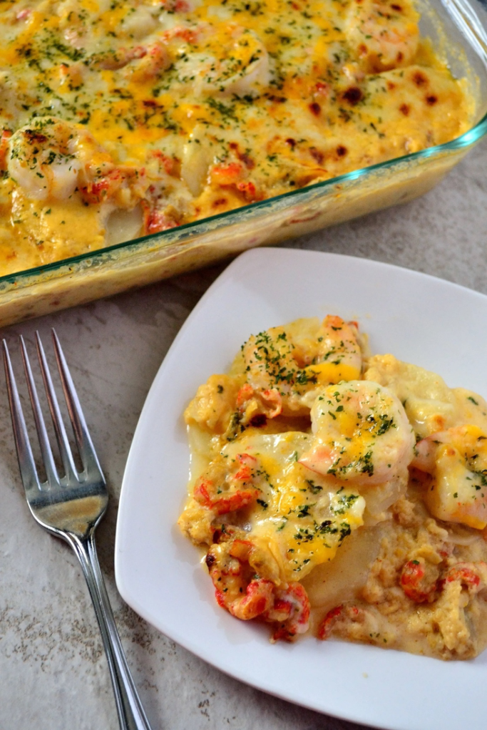 Seafood Potatoes Au Gratin on a white square plate with casserole dish and fork in the background