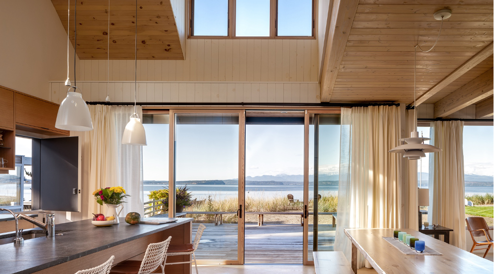 A sweeping view of the Salish Sea and Olympic Mountains from main living space of this beach cabin on Mutiny Bay, Whidbey Island, WA, designed by Seattle firm Graham Baba Architects