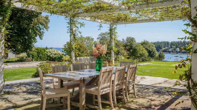 coastal patio with dining area under a pergola covered with greenery, ocean background