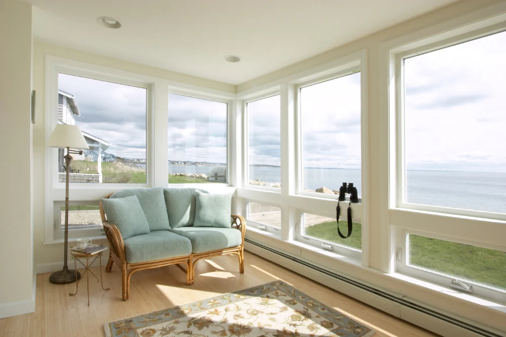 beach home sunroom facing ocean with a pair of binoculars on the window ledge to illustrate Schedule Renovations Around Coastal Weather Patterns